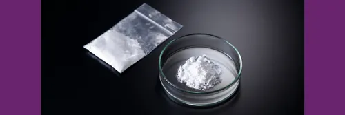 White powder in a dish and in a small plastic bag sit on a black surface